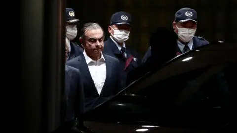 AFP Carlos Ghosn is escorted as he walks out of the Tokyo Detention House following his release on bail in Tokyo in April 2019