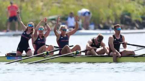 PA Media Five rowers celebrate in their boat after winning their final at the Paris 2024 Paralympics. The crew of three women have their arms aloft, while the two men at the rear of the boat are facing downwards as if recovering from their efforts.