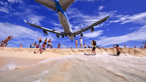 Princess Juliana Airport A low-flying plane with blue livery passes overhead on a beach at Princess Juliana airport, Sint Maarten