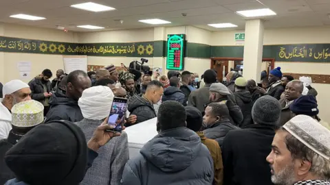 A group of people around a coffin inside a mosque