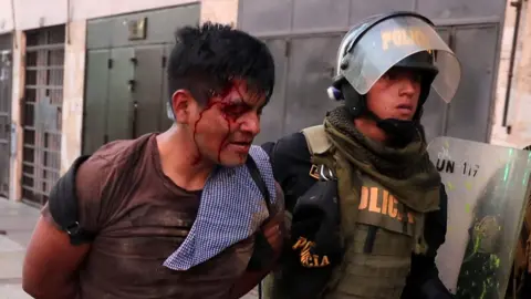 A protester with blood on his face being taken away by police in riot gear