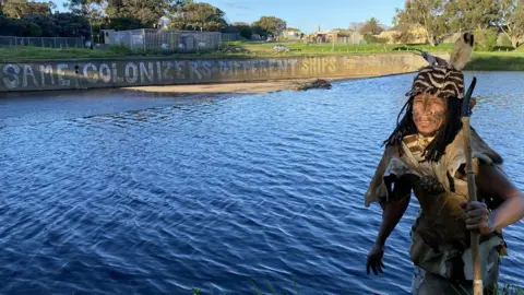 Man in traditional dress standing in front of some water