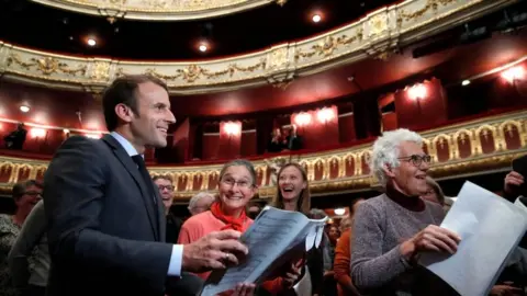 President Macron smiles as he joins a group of women during a rehearsal at an Opera