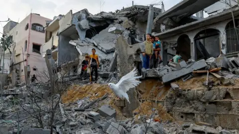 Reuters A dove flies over the remains of buildings destroyed in Israeli air strikes in Khan Younis, in the Gaza Strip (11 October 2023)