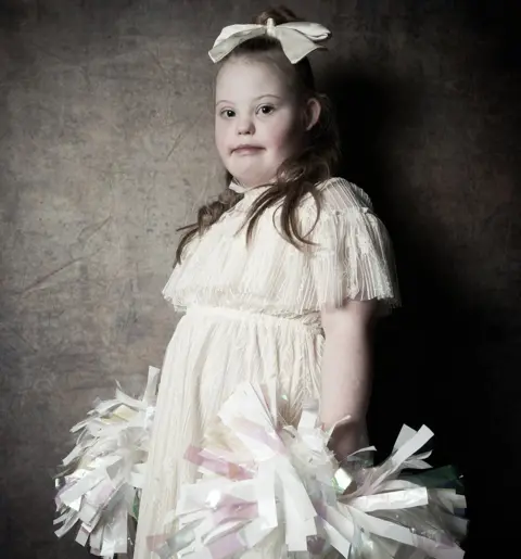 Debbie Todd Maisie, aged eight, wearing a white dress and holding two large pom poms