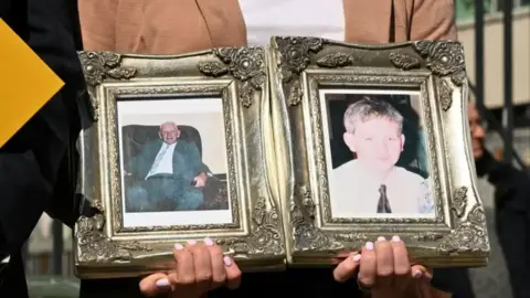 Pacemaker Hands holding two framed photos of two men - Kevin and John McKearney. The picture frames are gold and ornate.