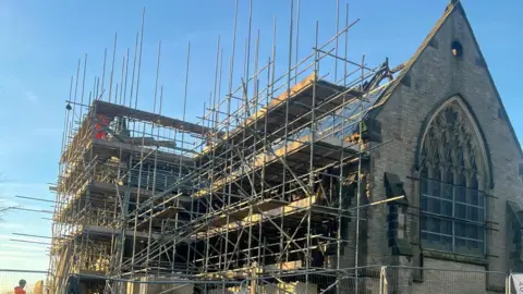 Ushaw Scaffolding surrounding the outside of the chapel. It has a big stained glass window on the side in the shape of an arch.