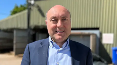 BBC/James Ingham MP Andrew Griffith, wearing a light blue shirt and blue jacket, looks at the camera outside the abattoir.