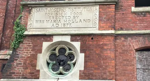 Exterior shot of St Joseph's orphanage with stained-glass window and carved foundation stone