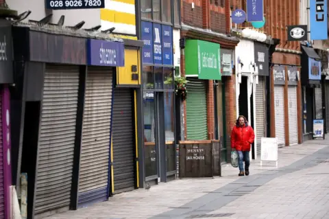 PA Media A man walks past closed shops on a street in Belfast city centre
