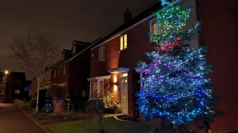 BBC Christmas tree with lights on outside of a house.