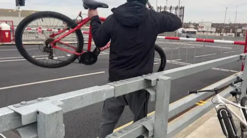 Andrew Turner/BBC Man lifting his bike over a barrier