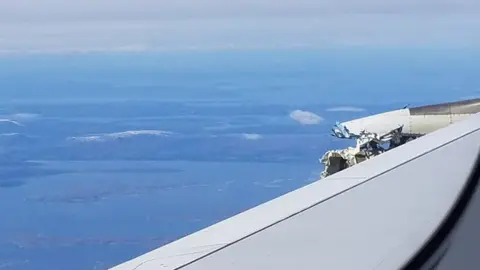 David Rehmar A view over the wing, showing land in the distance beyond, while the plane is still airborne. Mangled metal can be seen poking above the surface.