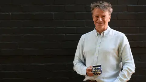 Anglia Ruskin University Prof Saul Humphrey smiling and holding a cup