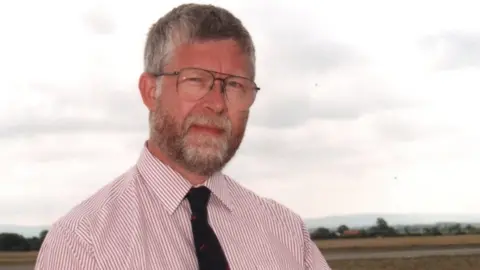 Brian Wright A man in a shirt and tie with a brown and grey beard and glasses