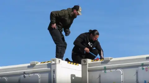 National Crime Agency Florjan Ibra (left) and Arman Kaviani (right) pictured on top of the container