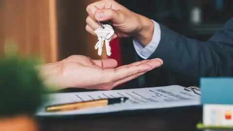 Getty Images/Natee Meepian Estate agent giving house keys to woman (stock photo)