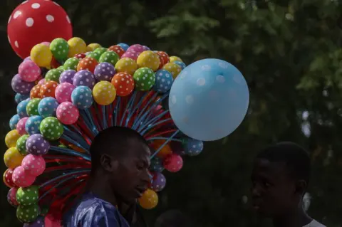 KOLA SULAIMON/AFP A Nigerian balloon vendor displays his wares at the celebration of the wedding of 1800 couples at Kano Central Mosque, Kano State, Nigeria on October 13, 2023. The mass wedding is sponsored by the Kano State government in Nigeria to help widows and divorcees get remarried.