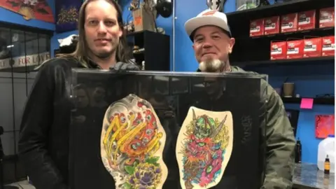 Courtesy Cheryl Wenzel Tattoo artists Kurt Wiscombe (left) Clint Danroth with the preserved tattoos they did for Chris Wenzel