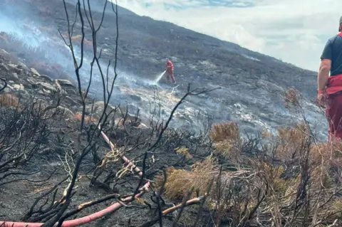 Derbyshire Fire and Rescue Service Burnt moorland with a firefighter spraying water on the ground.