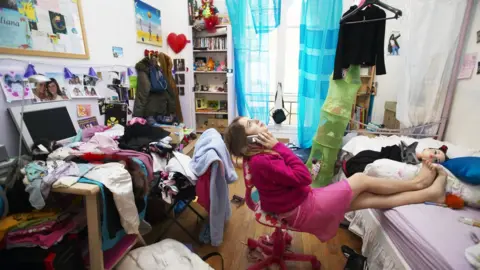 Getty Images A woman sitting on her phone in a messy room.