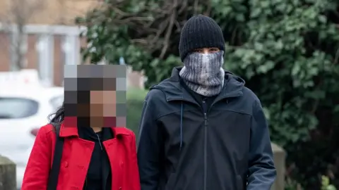 Bradley Page Photo of PC Hussain Chehab wearing a hat and a scarf pulled up over his mouth and nose, pictured with an unidentified woman.