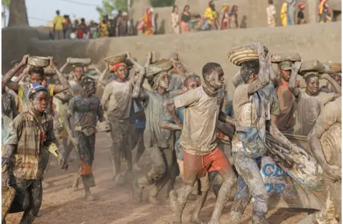 Ousmane Makaveli/AFP A crowd of people on the move carrying mud buckets - 4 June. They have mud on their bodies.
