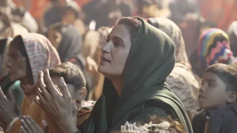 Kamil Khan Woman claps hands surrounded by other women and children attending a Christmas carol concert