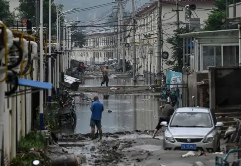 Getty Images Residents clean up the street in the aftermath of the flooding at a village following heavy rains in Beijing on August 3, 2023.