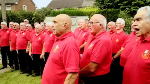 PEOPLECANRUN.COM More than 20 members of Aber Valley Male Voice Choir snuck into Emlyn's garden