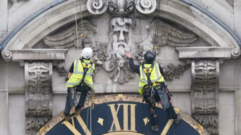 PA Media Adam Garre and and Lewis Head work carefully above the clock face