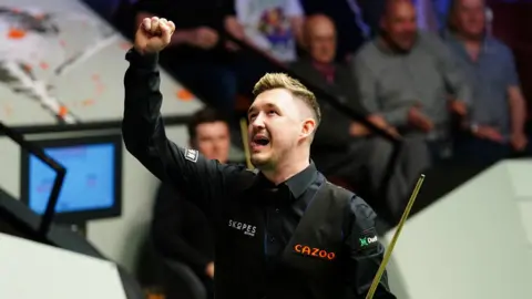 Mike Egerton Kyren Wilson wearing black shirt with his arm in the air in front of an audience.