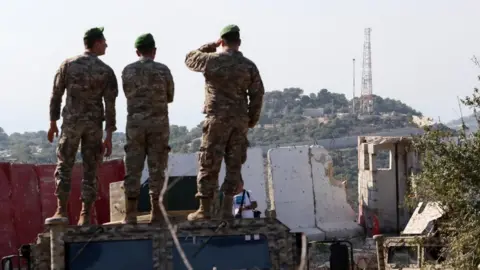 Three Lebanese soldiers stand on top of a vehicle with their backs towards the camera as they look towards a hill in the distance (file photo)