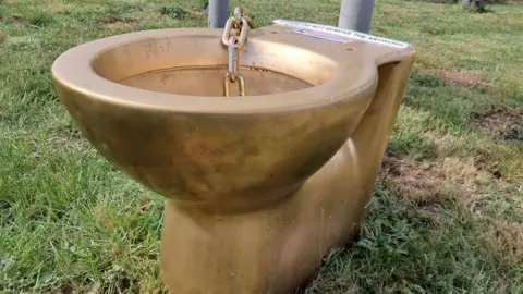 BBC A close up on the gold toilet, sitting on some grass