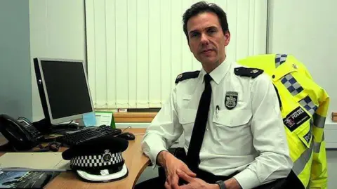 A man in a police uniform sat down with his hat on a computer desk.