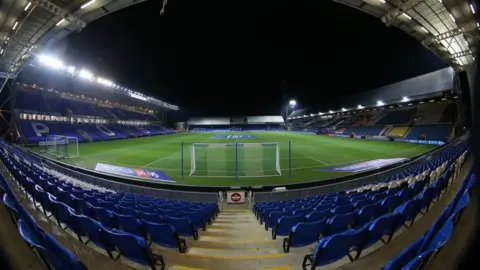 PA Media A wide view shot of the interior of the Weston Homes Stadium in Peterborough. It shows the blue seats behind one of the goals beyond which you can see the length of the pitch.