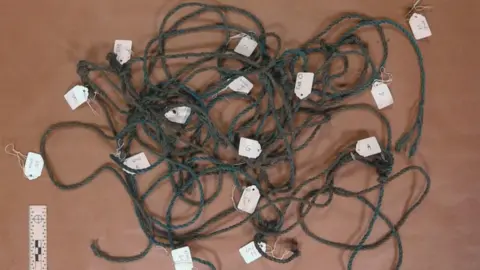 Avon and Somerset Police A close up image showing coiled up blue plastic rope lying on a brown surface - a key piece of evidence in the investigation. The rope is long but is made up of individual pieces tied together. There are small white tags indicating where each length of rope ends. 