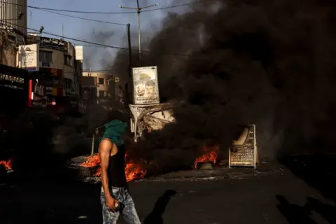 Ronaldo Schemidt / AFP A masked man walks near a fire during clashes with the Israeli army in the occupied West Bank city of Jenin