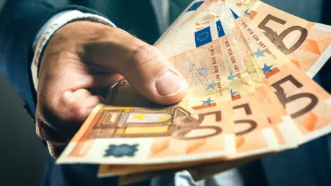 Getty Images A stock image shows a man holding a handful of €50 notes out in offering