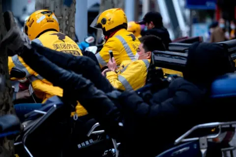 Getty Images Motorcycle delivery workers wearing protective facemasks wait for orders along a street in Shanghai.