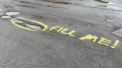 BBC/Naj Modak Graffiti next to potholes on the road