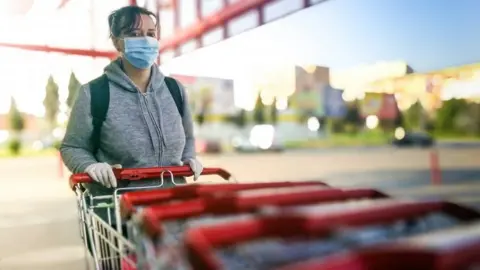 Getty Images Woman in mask and gloves pushing shopping trolley