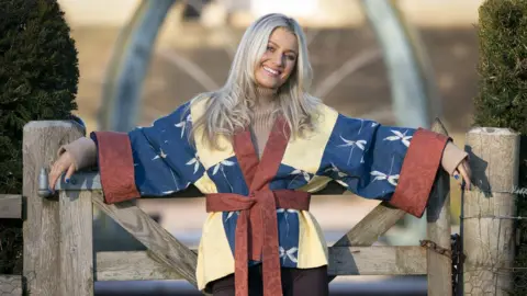 PA Media woman wearing red, yellow and blye kimono, standing next to gate