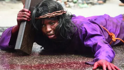 A man lies on the ground carrying a crucifix during a dramatisation of the crucifixion of Jesus Christ to mark Good Friday, heralding the start of Easter celebrations, in Lagos on March 30, 2018.