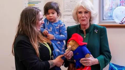 Camilla, the Queen Consort, holding a Paddington Bear toy and a marmalade sandwich