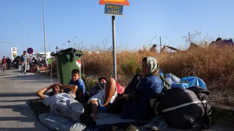 EPA Migrants sit on a roadside near the site of the camp