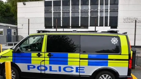 Pacemaker Press A police van is parked in front of Lisburn Court House. The windows are heavily tinted. The car is yellow and blue with POLICE in large lettering. The court house is painted white. 