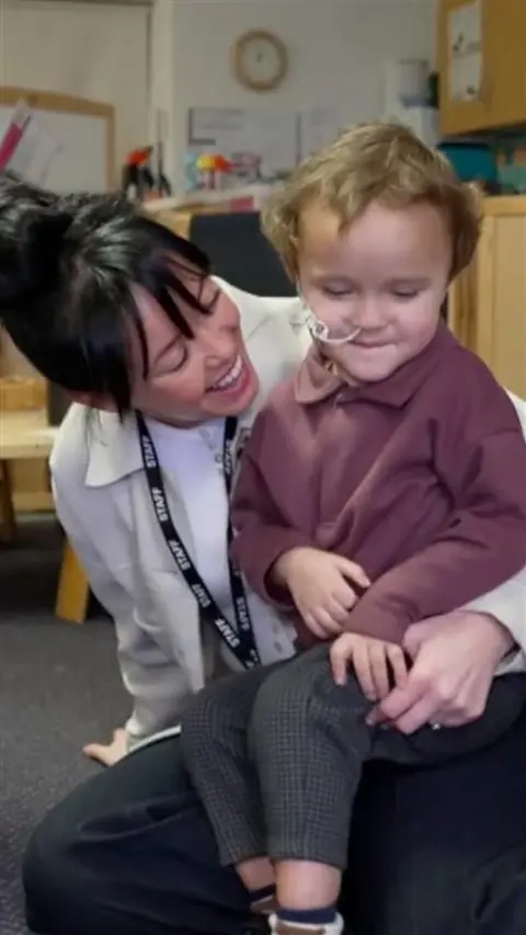 A young boy sat on the lap of a woman smiling with black hair.