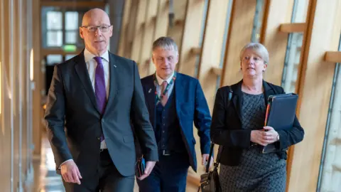 PA Media John Swinney and Shona Robison walking up a corridor in the Scottish Parliament