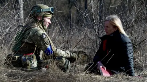 Goktay Koraltan / BBC Arthur sits on the bare, scrub-laden ground with Orla Guerin, talking